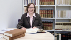 Prof. Dr. Christine Siegert (1971-2026) an einen Tisch sitzend und vor sich einige Bücher. Im Hintergrund Regale mit zahlreichen Büchern